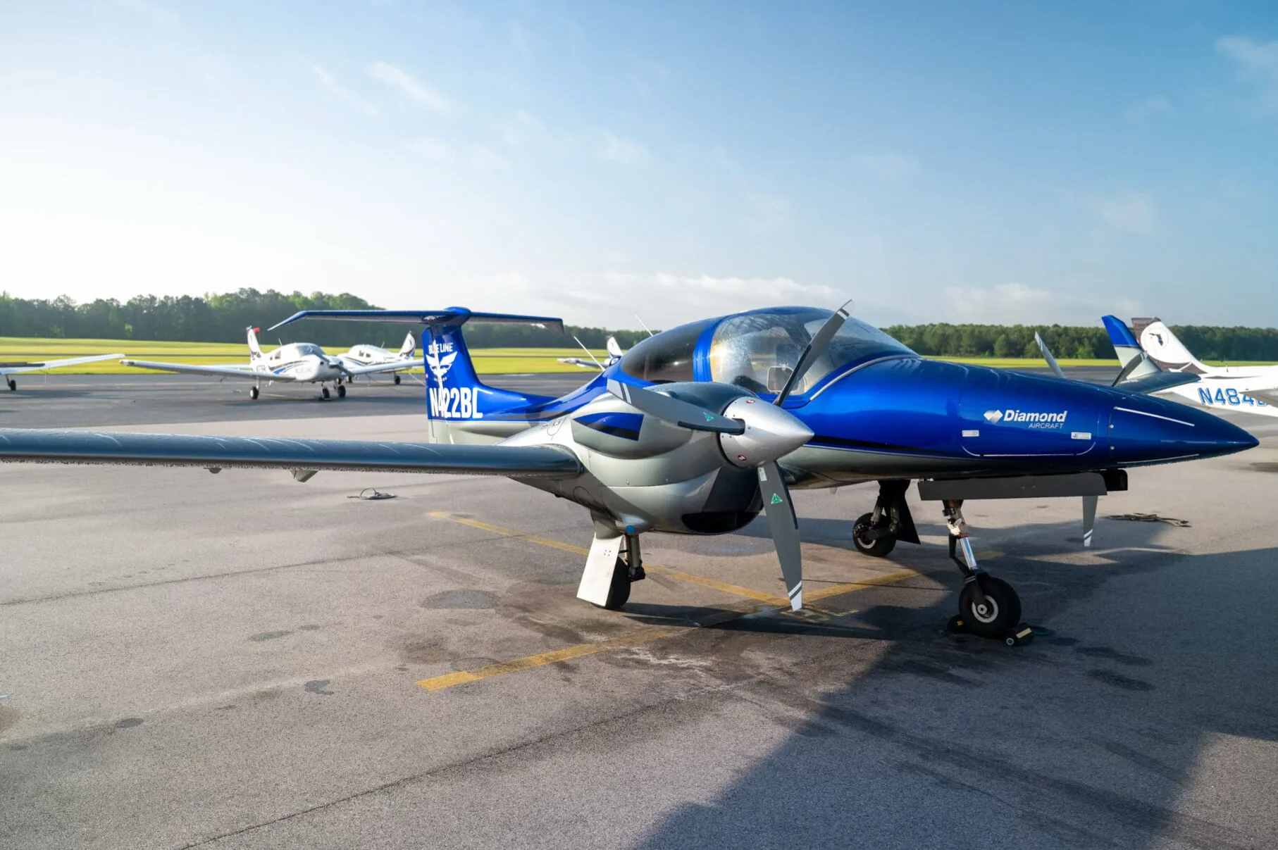A blue and grey Diamond DA42NG aircraft, N422BL, parked on an airfield with other planes in the background.