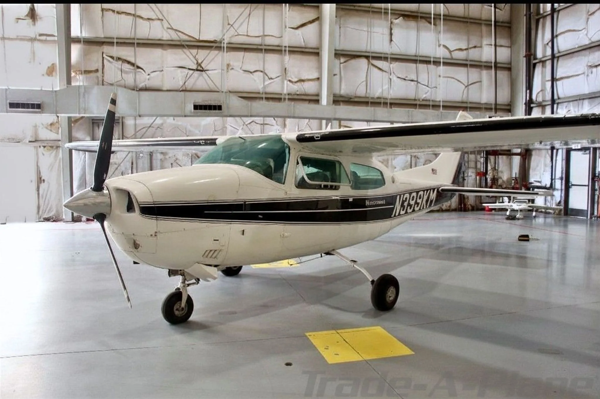 A white Cessna 210 Centurion with black stripes, seen from the front-left in a hangar.