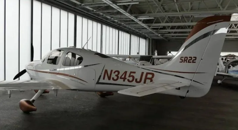 A white Cirrus SR22 aircraft with brown and silver accents, registration N345JR, parked in a hangar.