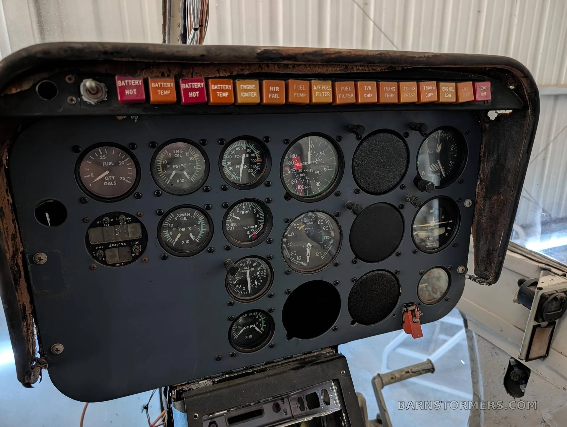 A close-up view of a helicopter's instrument panel, featuring various gauges and red warning lights.