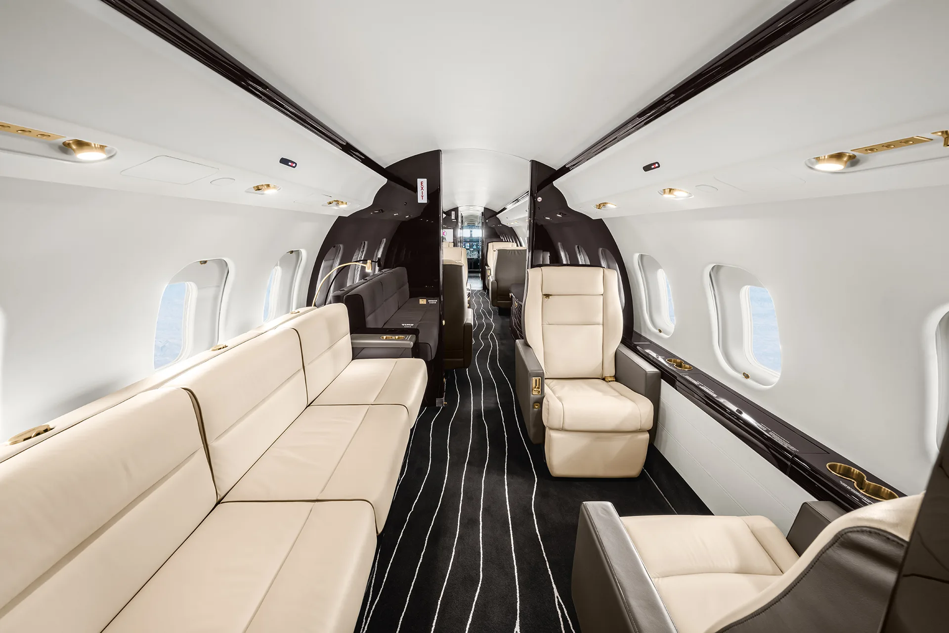A spacious private jet cabin interior with a long cream leather sofa on one side and individual cream seats on the other.