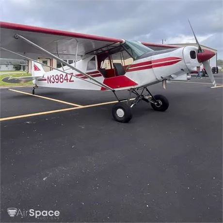 A white and red high-wing propeller aircraft, possibly a Piper Cub, with registration N3984Z, parked on an asphalt tarmac under a cloudy sky.
