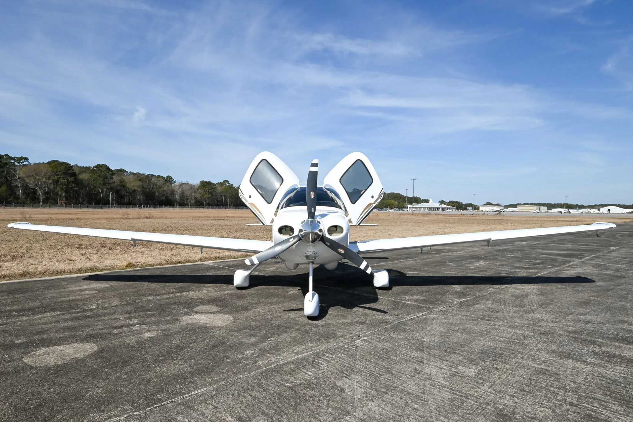 Front view of a white Cirrus SR20 aircraft with its doors open, parked on an airfield.