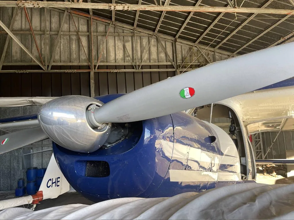 A close-up of the propeller and nose of a blue and white aircraft, D-EOAC, with an Italian flag decal on the propeller.