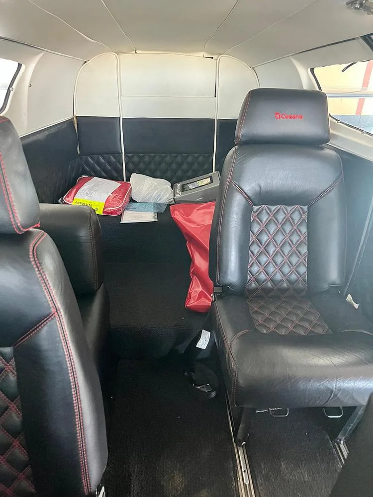 The aircraft's rear cabin interior with black leather seats, red stitching, and some items on the floor.