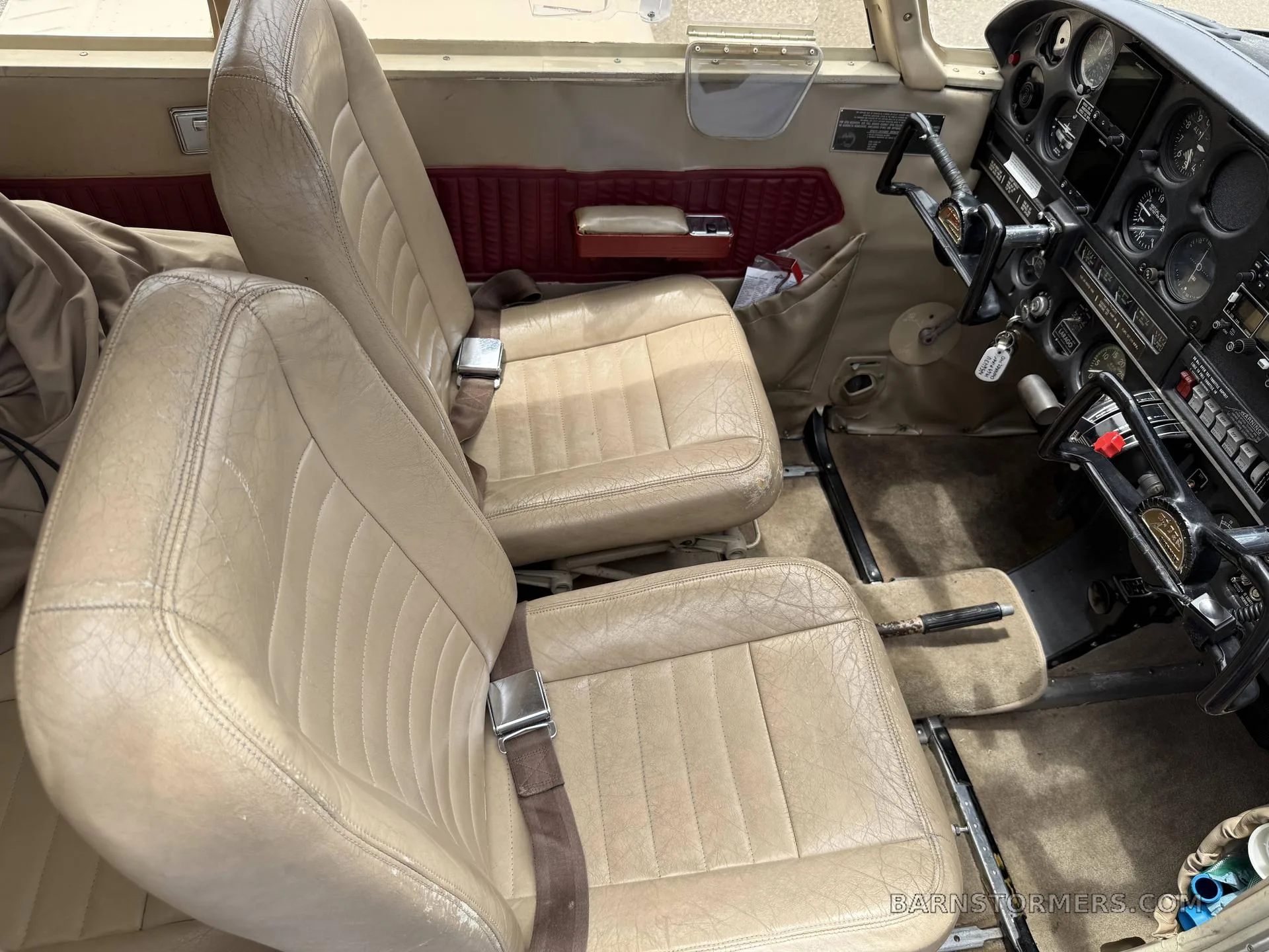 The front two tan leather seats of a small aircraft, with a partial view of the cockpit instruments on the right.