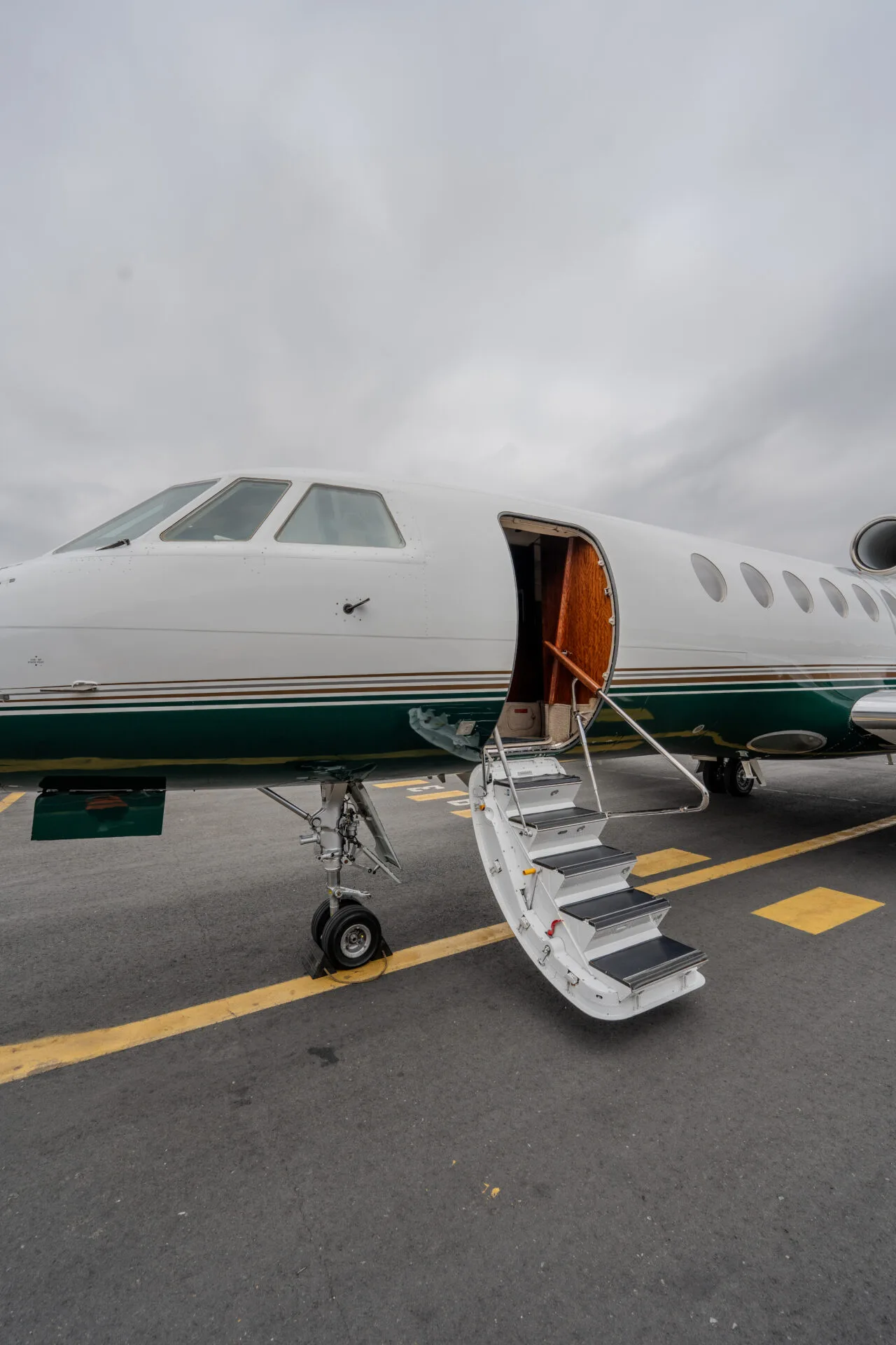 The front section of a white and green private jet with its main entry door open and stairs extended.