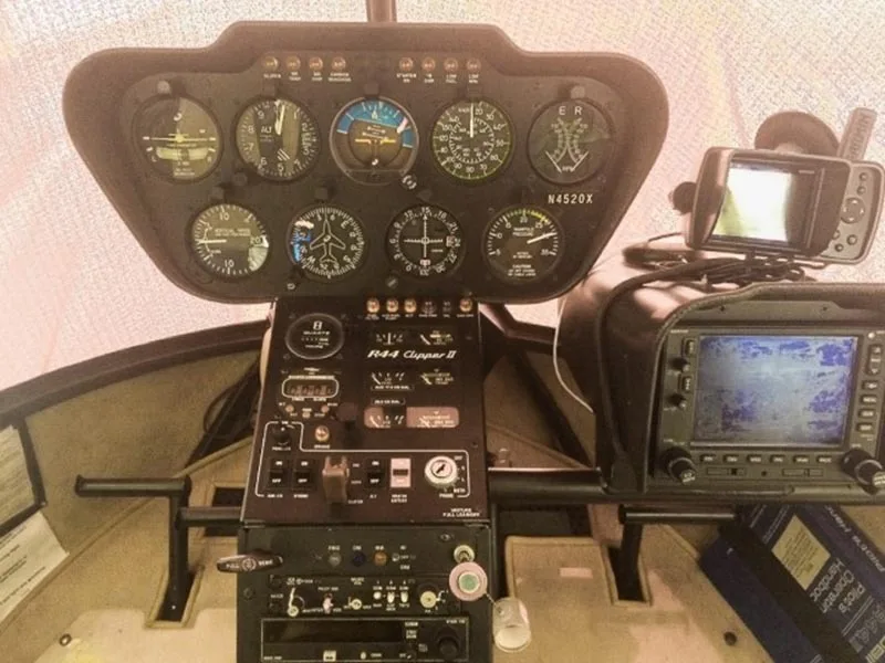 A close-up view of the Robinson R44 Clipper II helicopter's instrument panel, showing gauges, radio controls, and a mounted GPS unit.