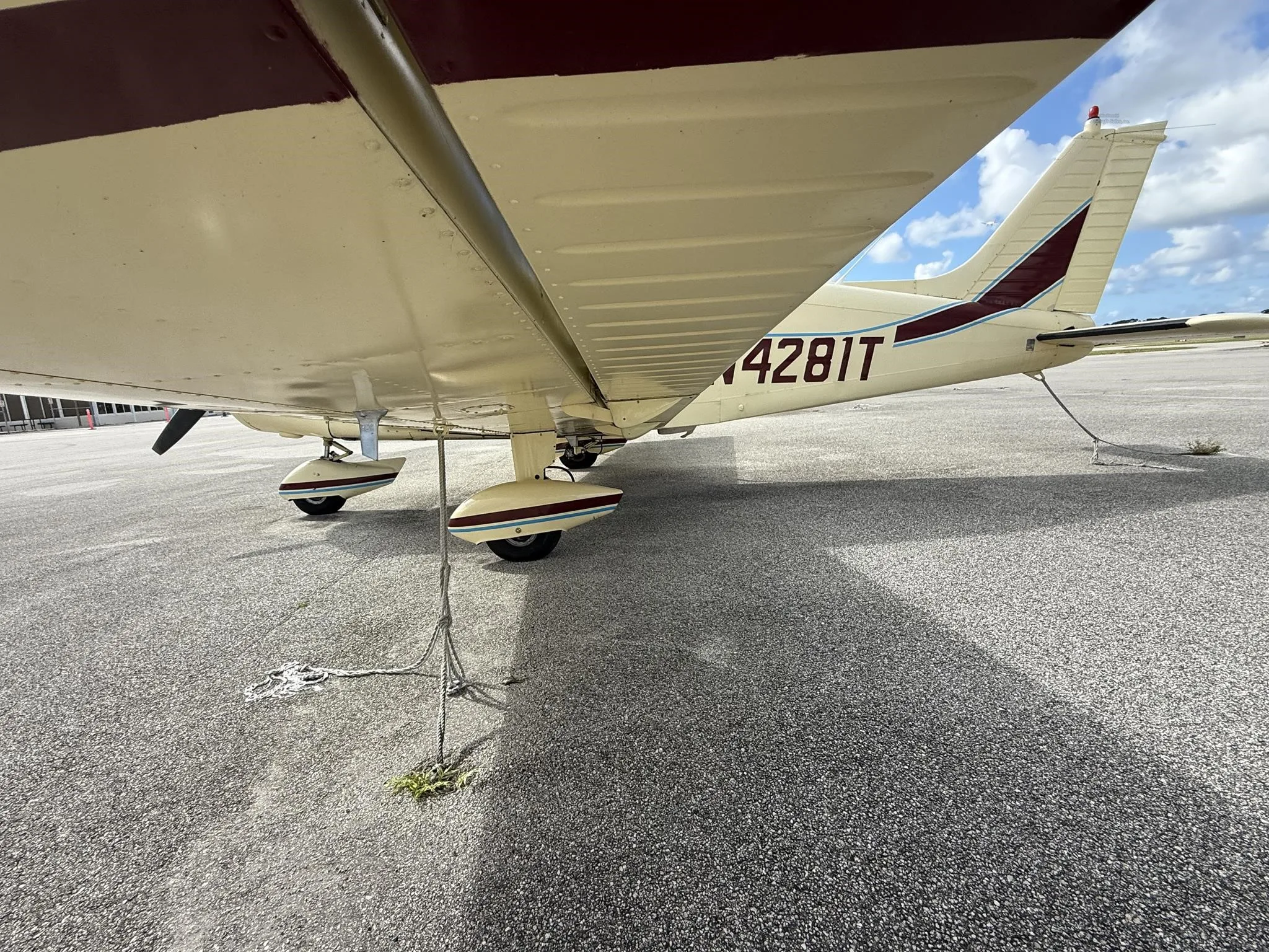 A close-up view of the landing gear and underside of the wing of a cream-colored Piper PA-28-140E Cherokee, registration N4281T.