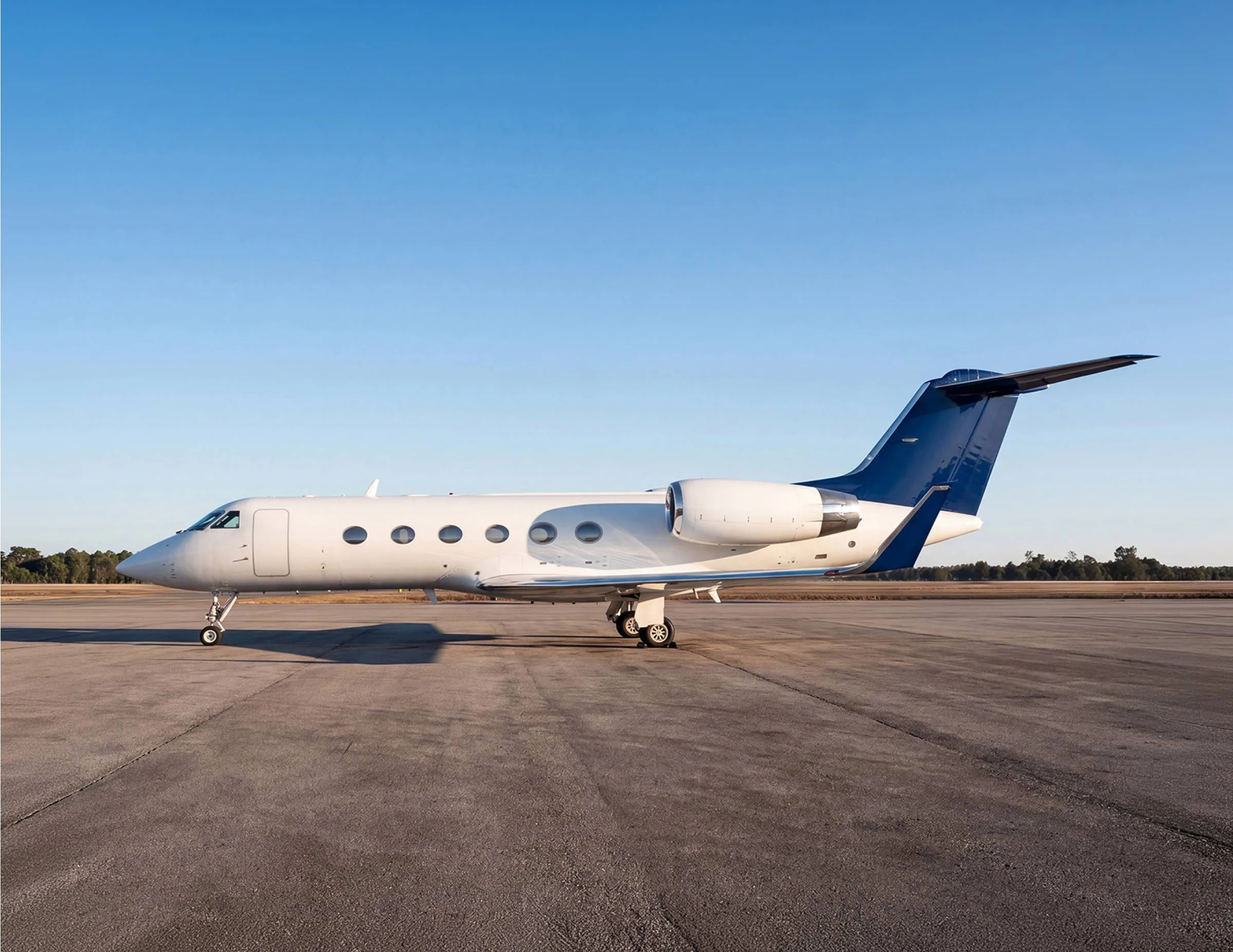 A white business jet with a dark blue tail parked on an airfield under a clear blue sky.