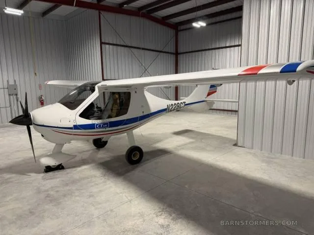 A white CTLS light sport aircraft with blue and red stripes on the tail and wings, parked in a hangar.