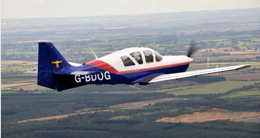 A white and blue single-engine propeller aircraft with red stripes and registration G-BDUG flying over a green landscape.