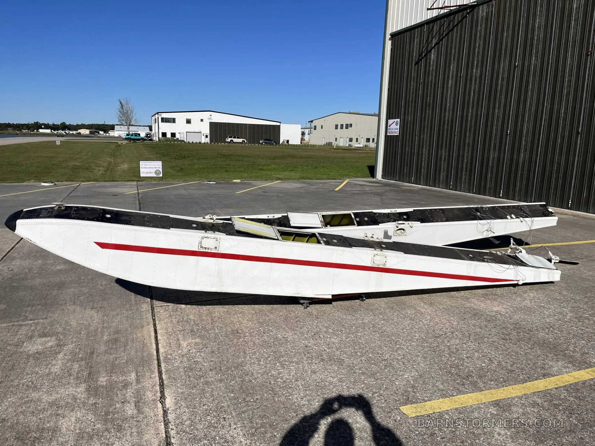 Two white aircraft floats with red stripes lying on a concrete apron next to a hangar.