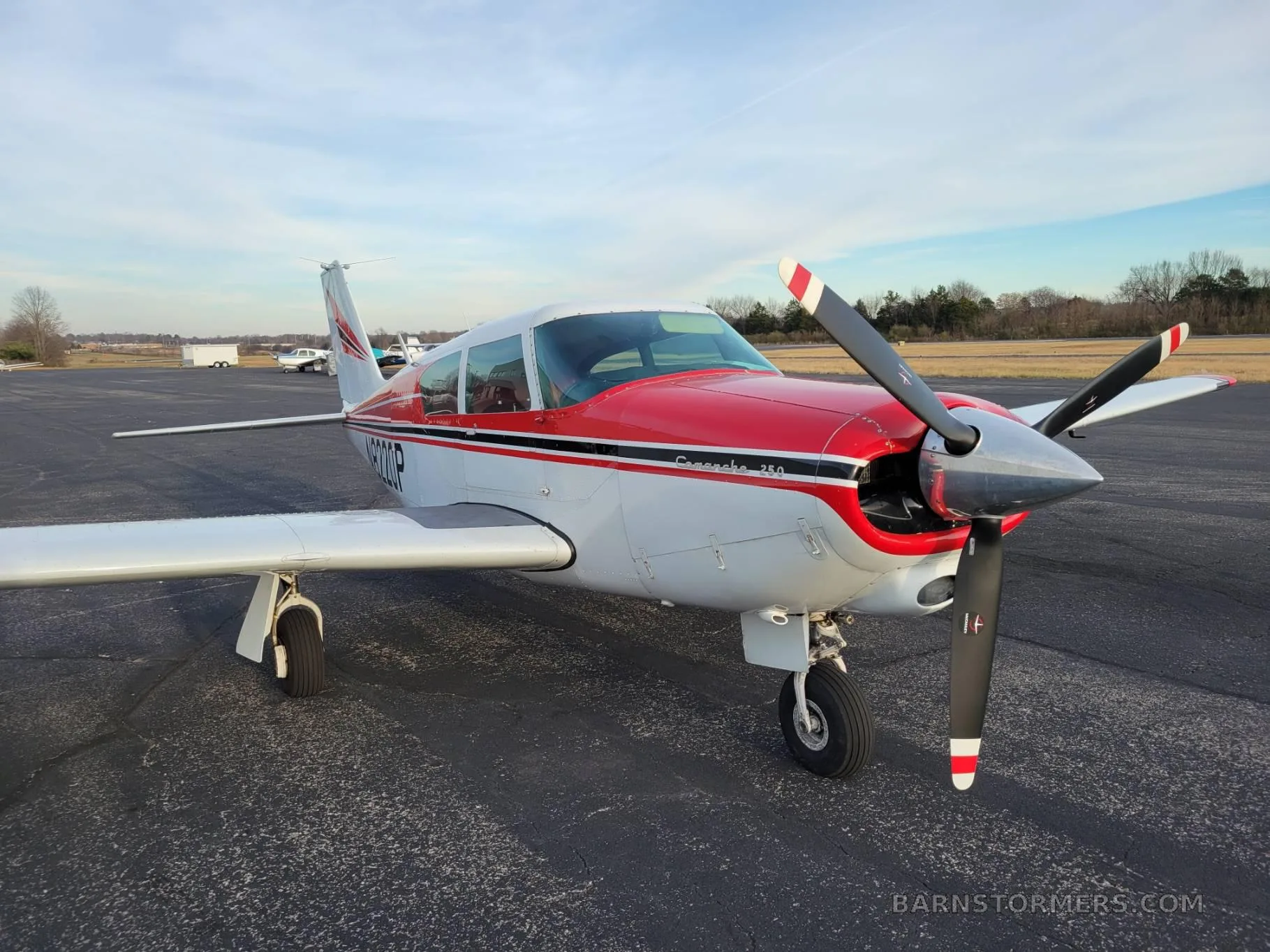 A white and red Piper Comanche 260 (N8220P) is parked on an asphalt ramp, viewed from the front-right.