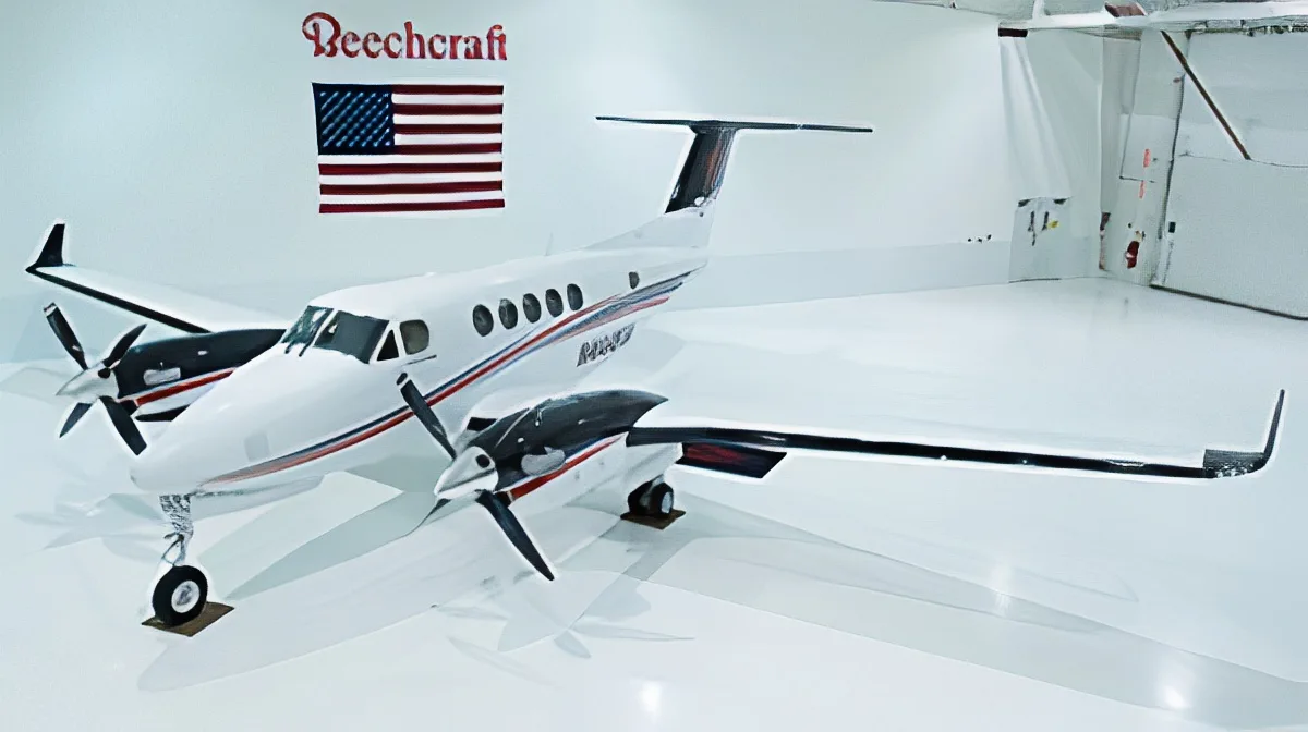 A white Beechcraft King Air twin-turboprop aircraft with black and red accents, parked in a clean white hangar with a Beechcraft logo and American flag on the wall.