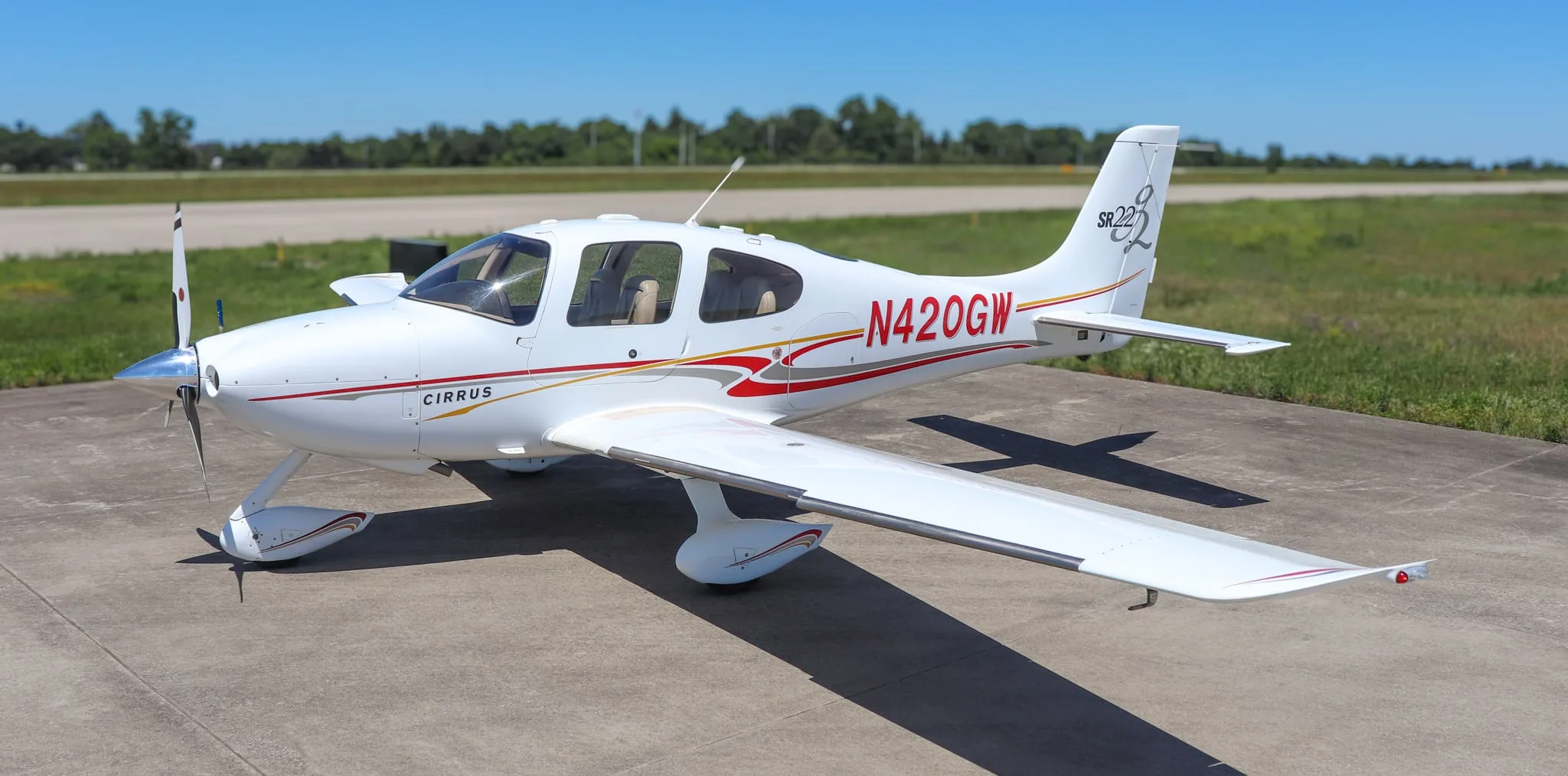 Top-down front-right view of a white Cirrus SR22 aircraft with red and gold stripes on a tarmac.