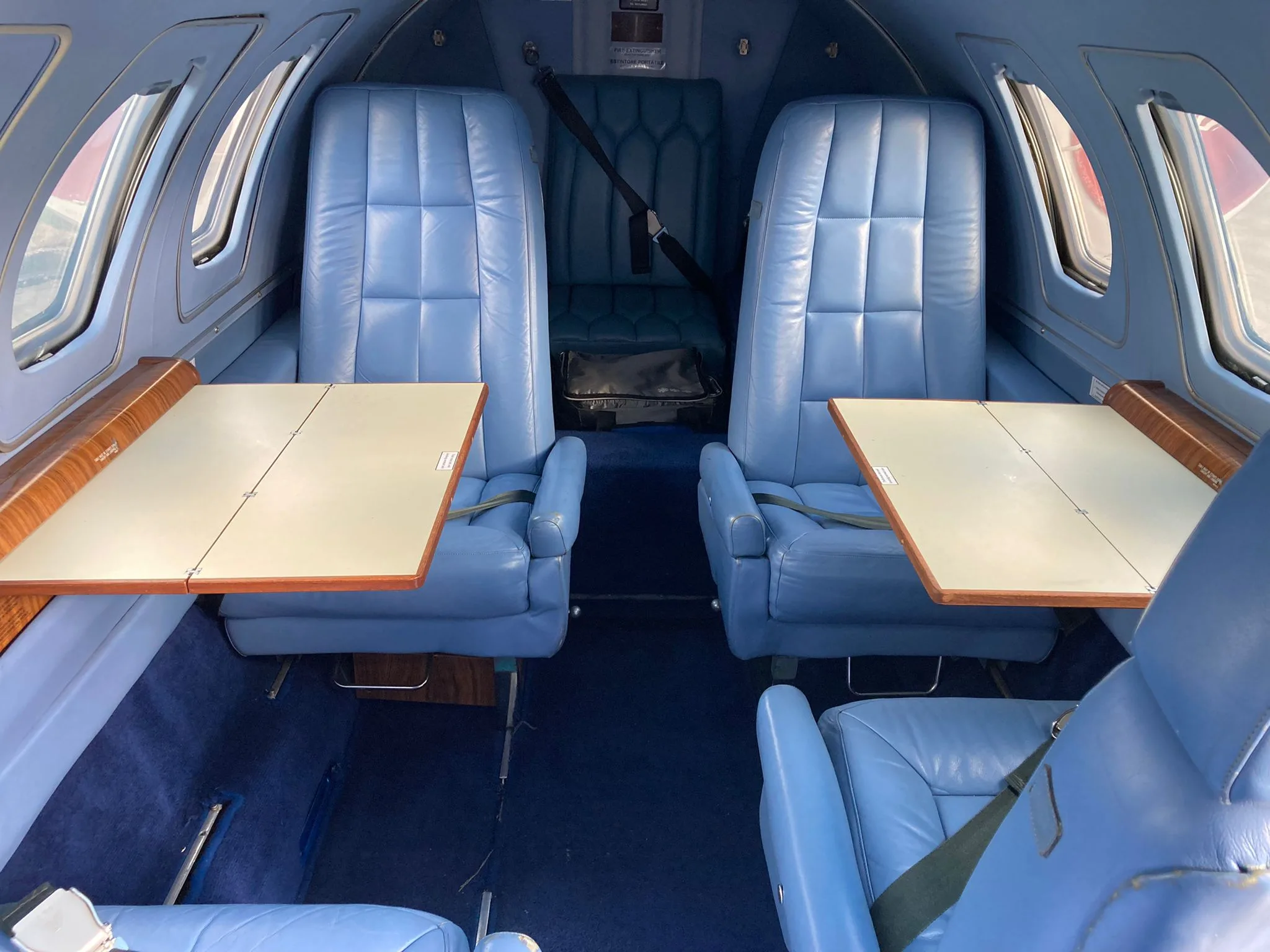 Interior of the aircraft with blue leather seats and fold-out tables.