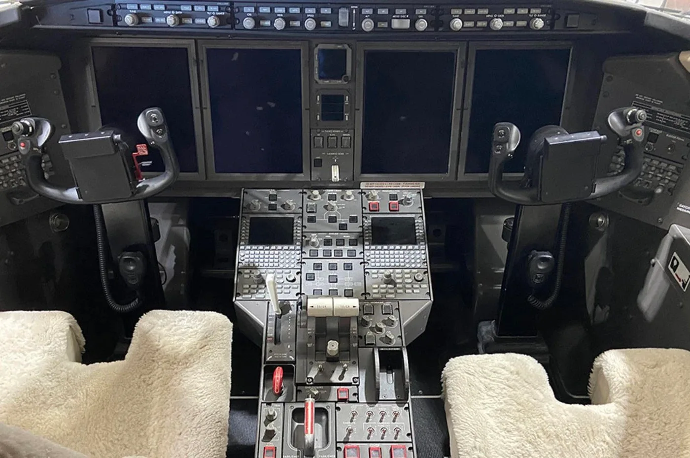 The cockpit of a business jet, showing the instrument panel with multiple screens, control yokes, and center console.
