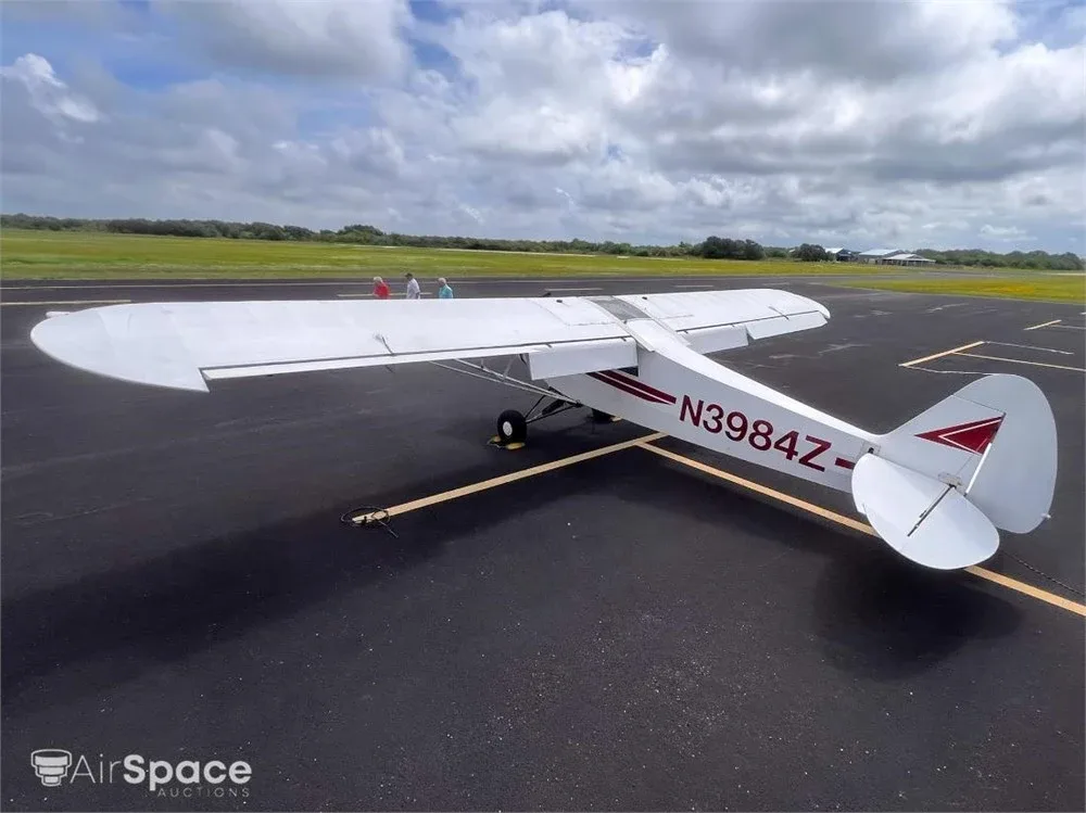 A rear-quarter view of the white high-wing aircraft N3984Z with red stripes, parked on an asphalt runway.