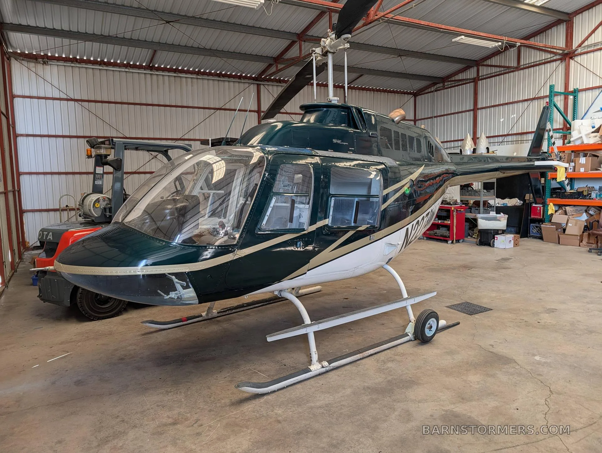 A dark green and white Bell 206 JetRanger helicopter with registration N2274W is parked inside a hangar.