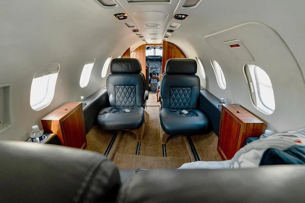 View from the rear of the aircraft cabin, showing two black leather seats and the cockpit entrance beyond.