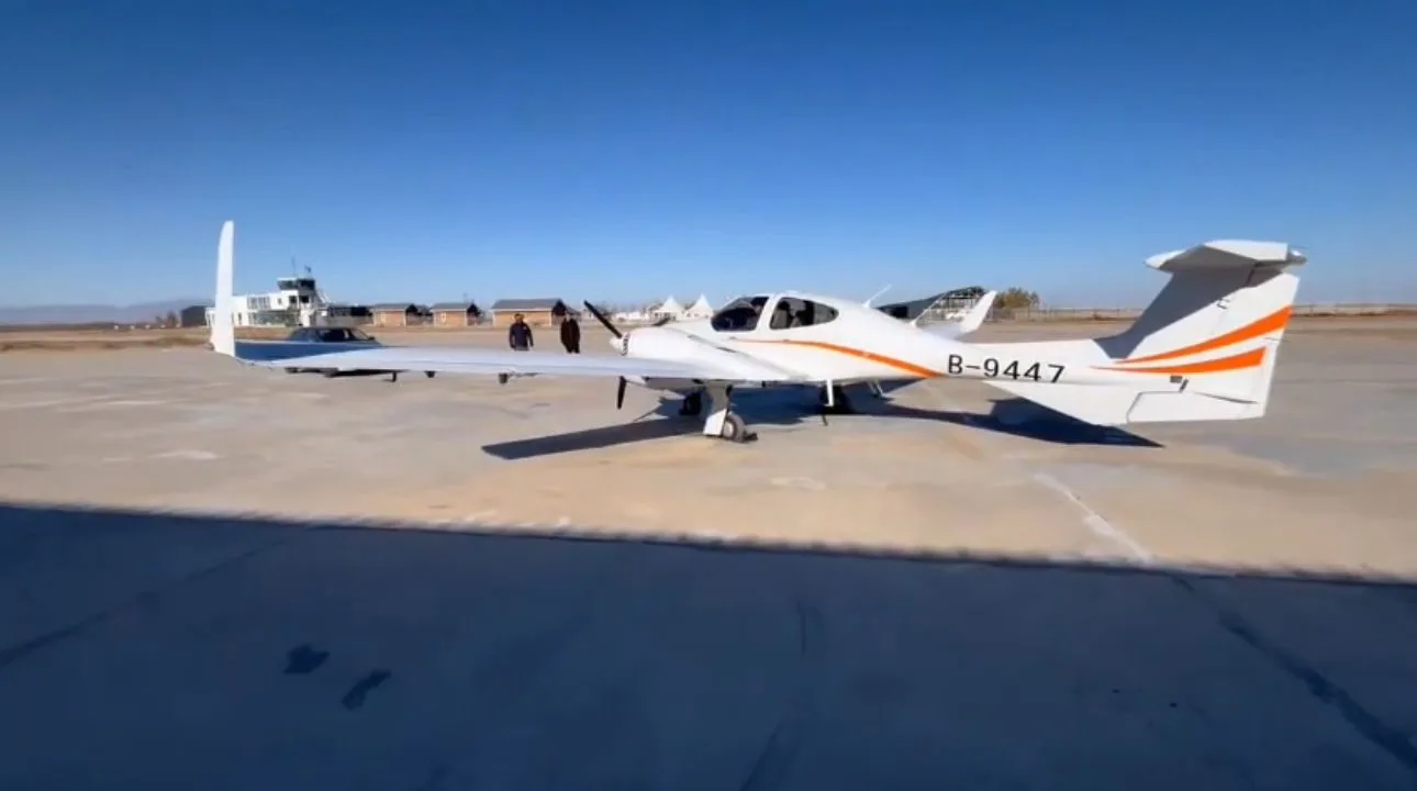 Side view of a Diamond DA42 aircraft parked on the tarmac with people standing nearby.