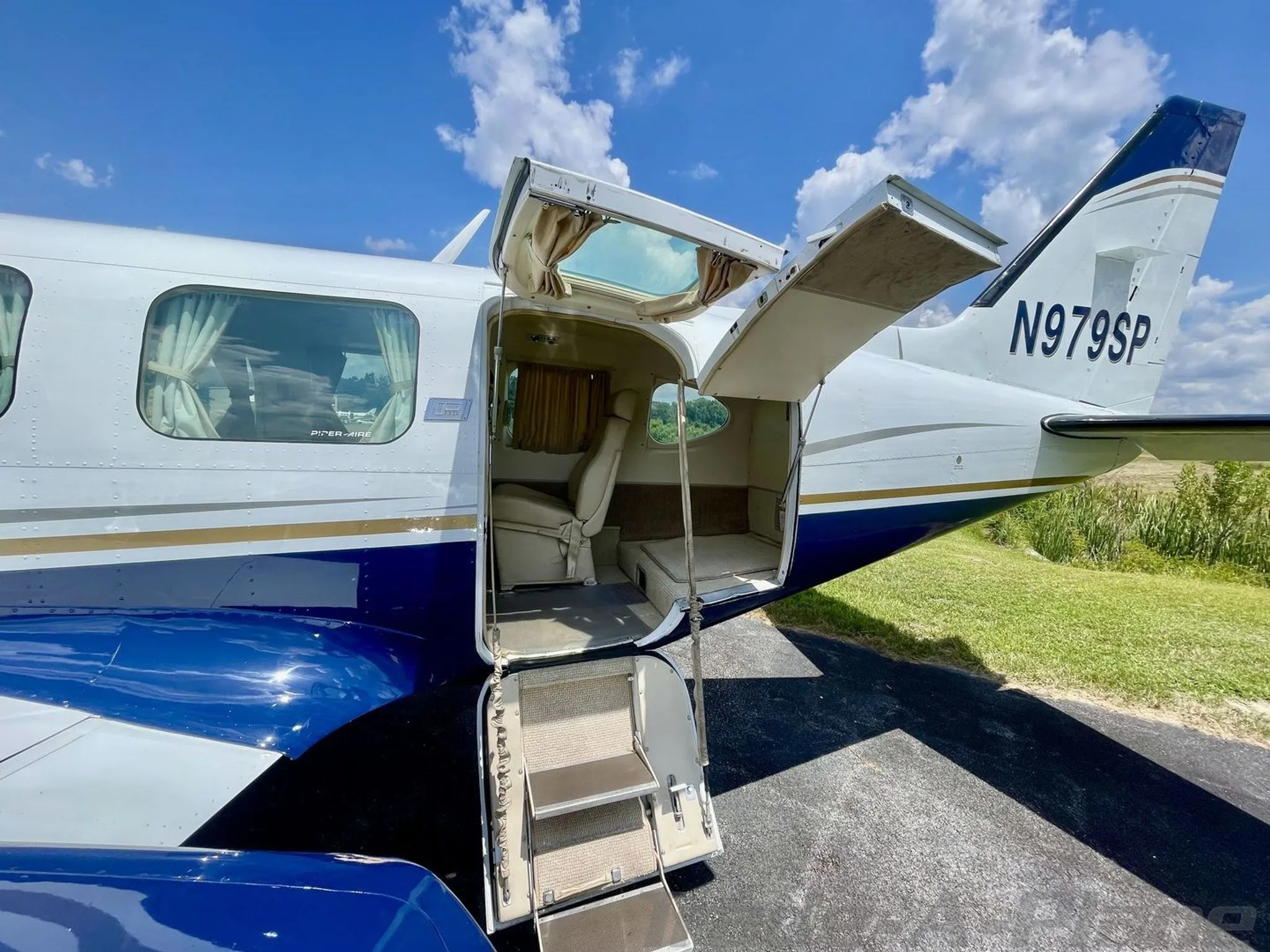 The cabin door of the white and blue Piper aircraft, N979SP, is open, showing the entry steps and a glimpse of the beige interior.