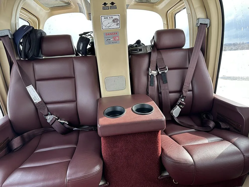 The rear passenger cabin of a helicopter with two brown leather seats and a center console with cup holders.