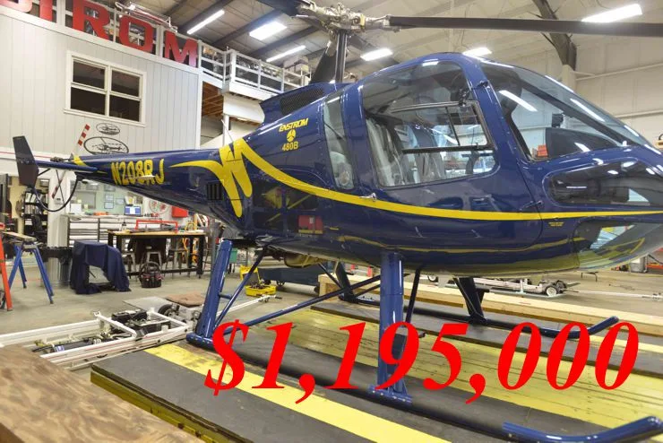 A blue Ekstrom 480B helicopter with yellow stripes and registration N208RJ is shown inside a hangar.