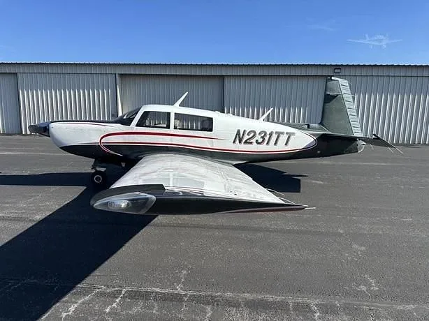 A white and dark-colored single-engine aircraft with tail number N231TT is parked on an asphalt ramp in front of a hangar.