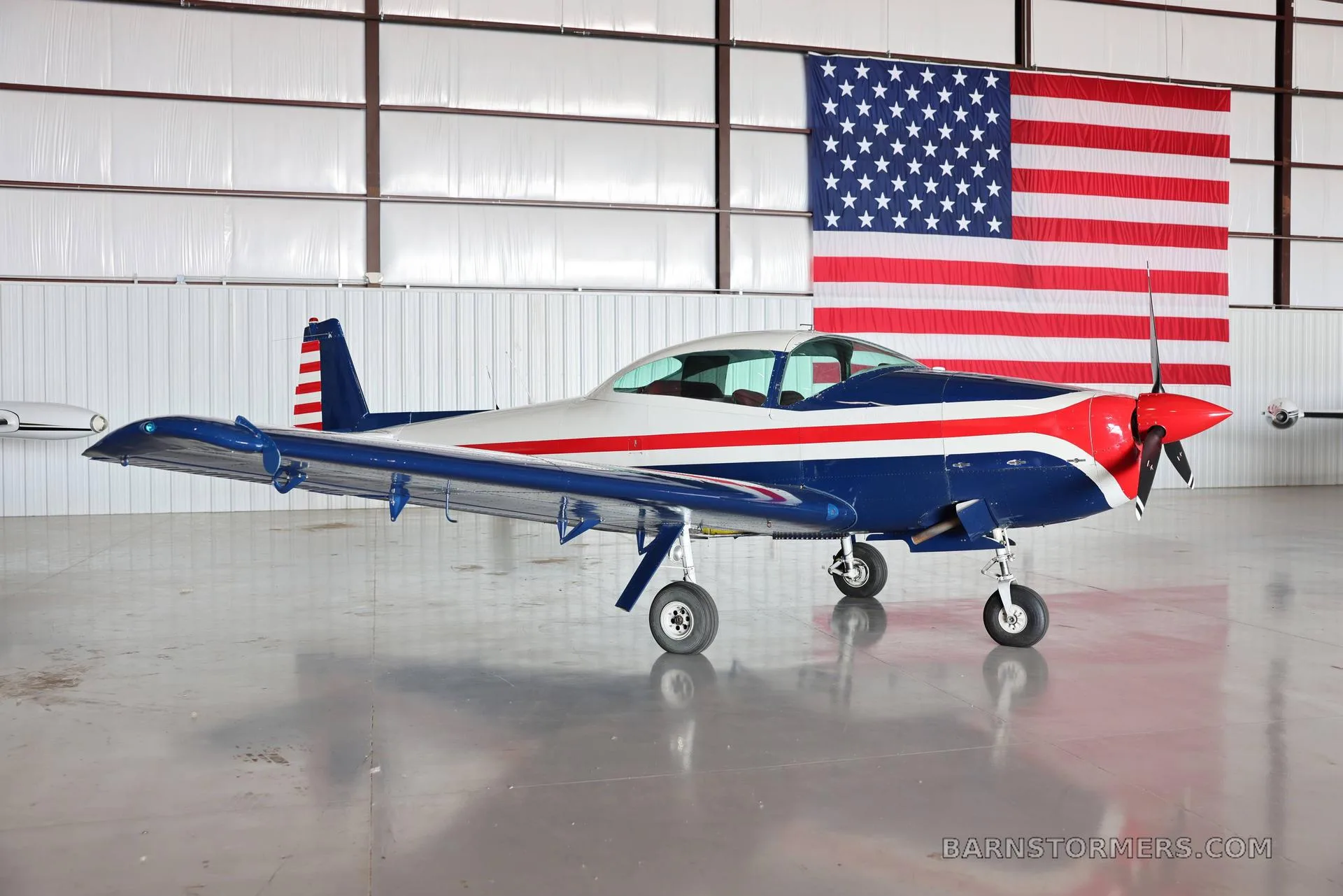 A blue, white, and red aircraft with an American flag in the background, parked in a hangar.