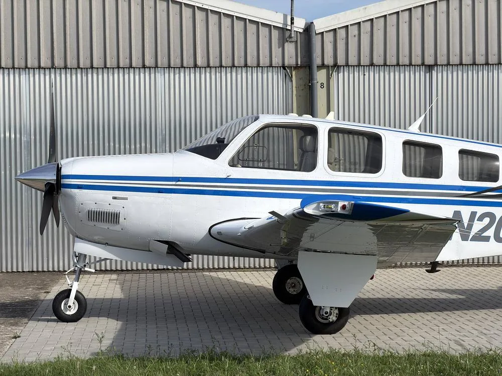 A close-up view of the front-left side of the white and blue Beechcraft Bonanza N205P, showing the propeller and landing gear.