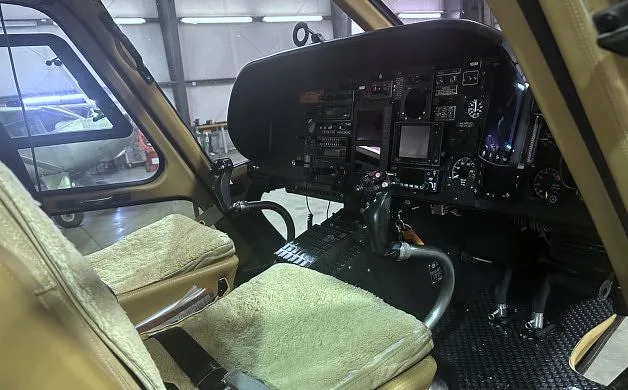 The cockpit of a helicopter features tan seats with sheepskin covers and a detailed instrument panel.