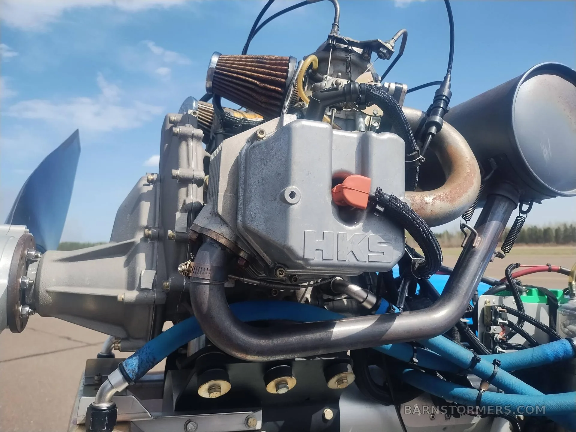 A close-up view of the HKS aircraft engine with its exhaust and air filter, against a blue sky.