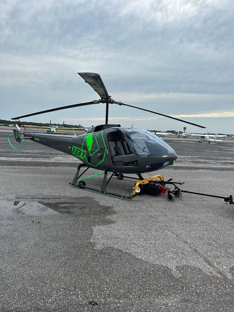A gray Enstrom helicopter with bright green accents and registration N88ZH parked on an airfield.