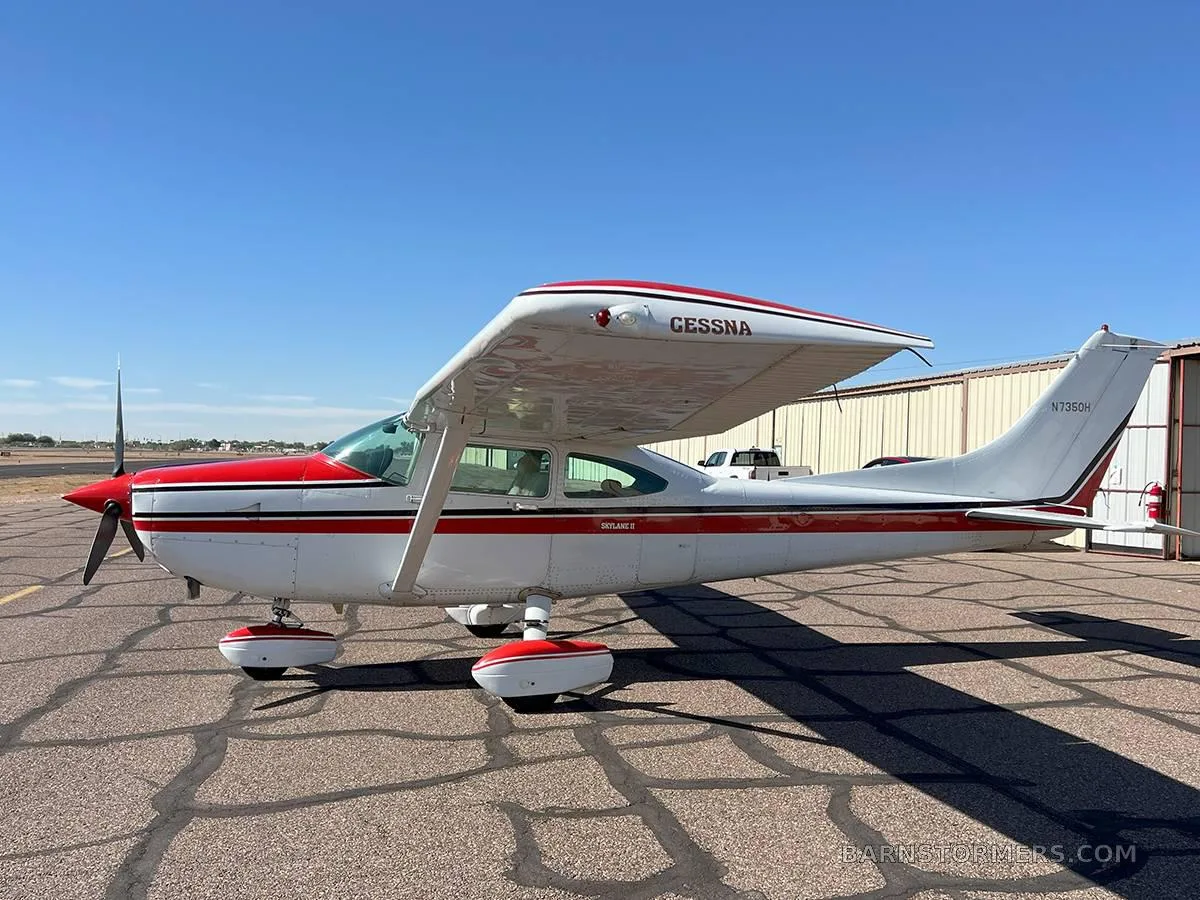 A white and red Cessna Skylane II aircraft is parked on an asphalt tarmac under a clear blue sky.