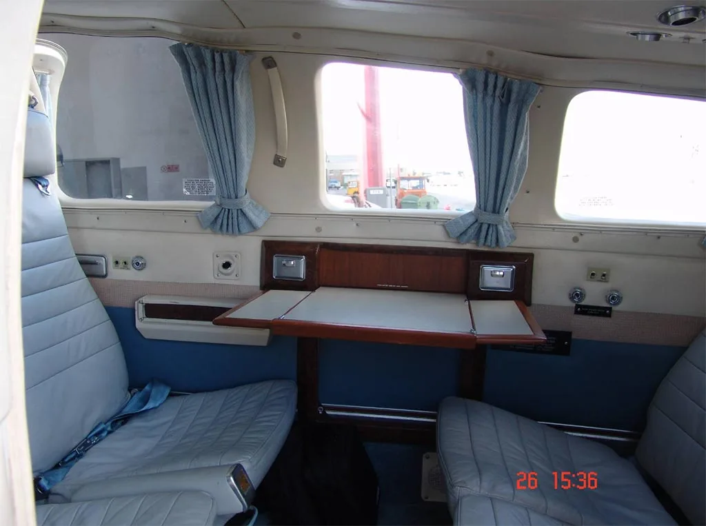 Interior view of an aircraft cabin with light blue seats, blue curtains, and a fold-out table.
