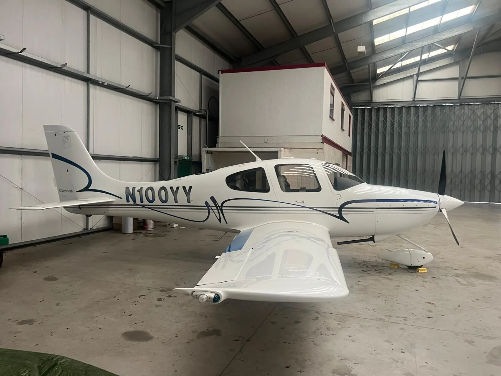 A white Cirrus SR22 aircraft with blue and grey stripes parked inside a hangar.