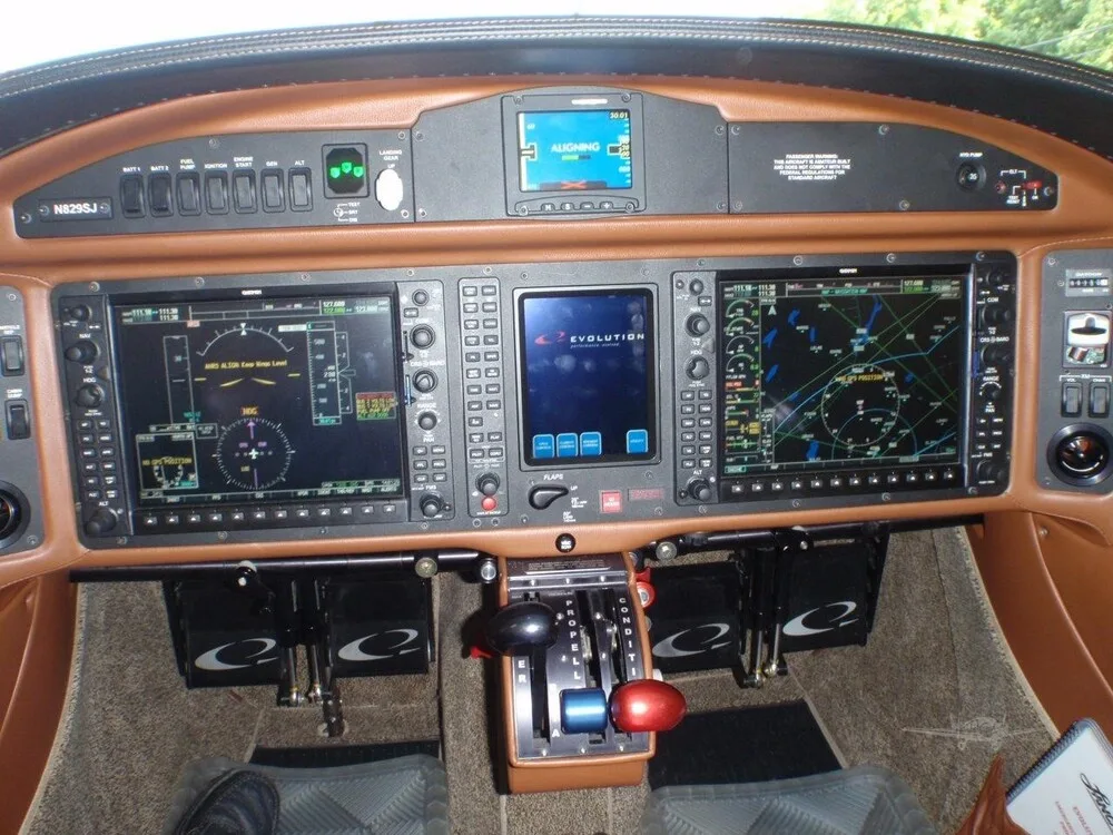 The cockpit of the N829SJ Lancair Evolution, featuring a modern glass panel with multiple displays and brown leather trim.