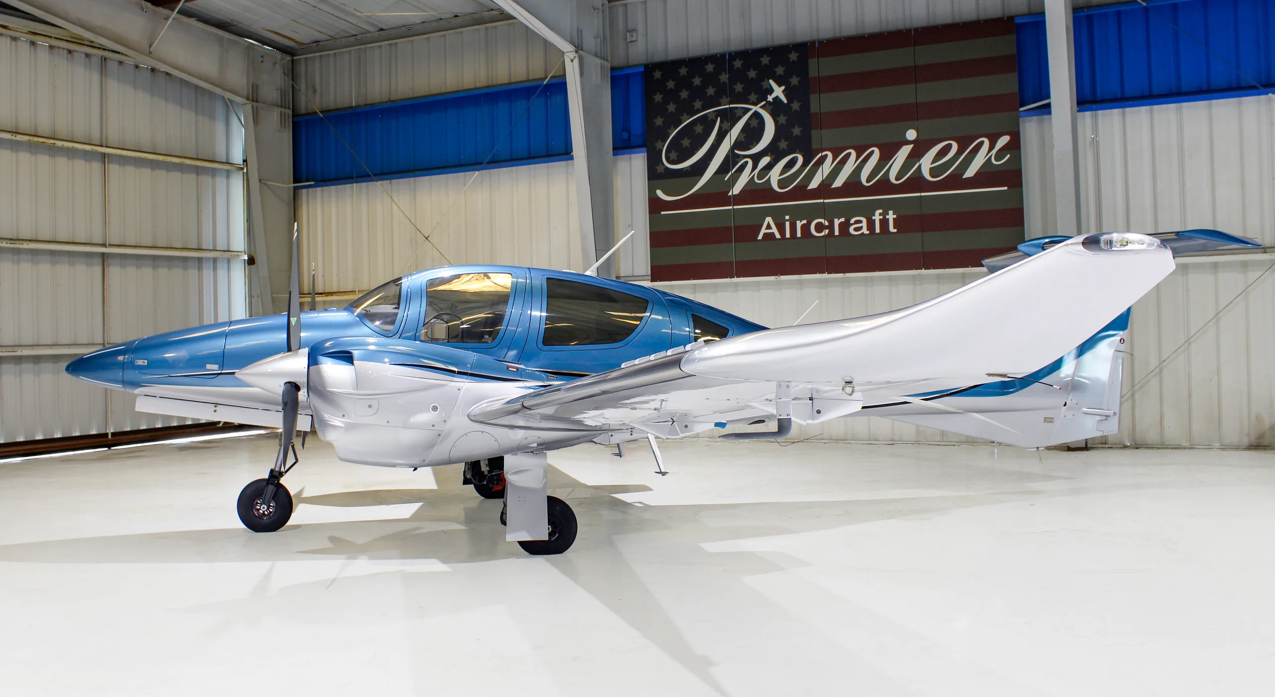 A side view of a blue and silver Diamond DA62 aircraft parked in a hangar.