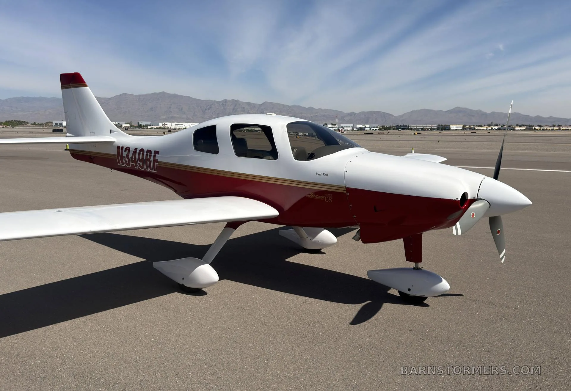 A white and red single-engine aircraft, N349RF, parked on an airfield with mountains in the background.