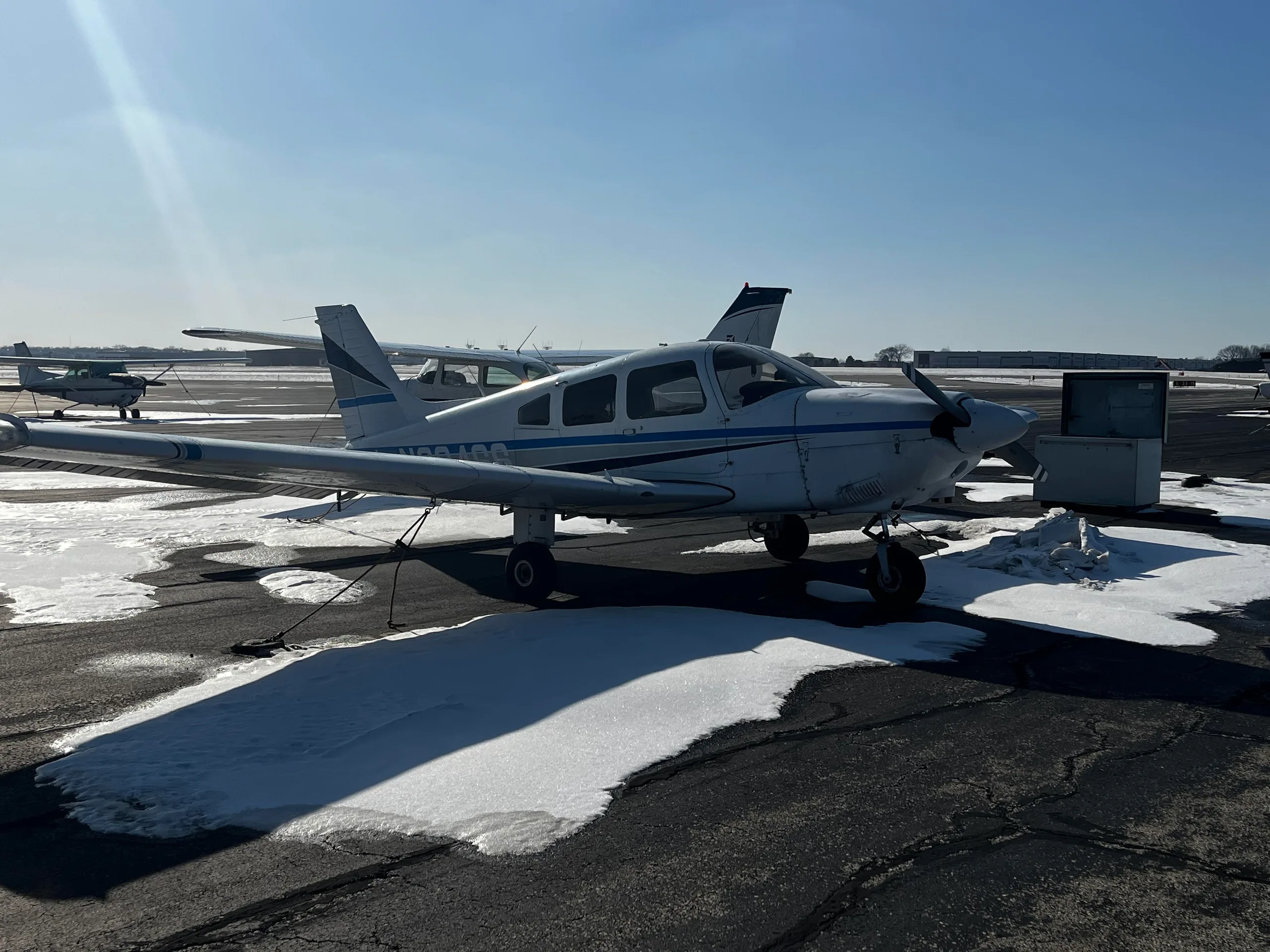 Side view of a white single-engine propeller aircraft with blue and grey stripes on a snowy tarmac.
