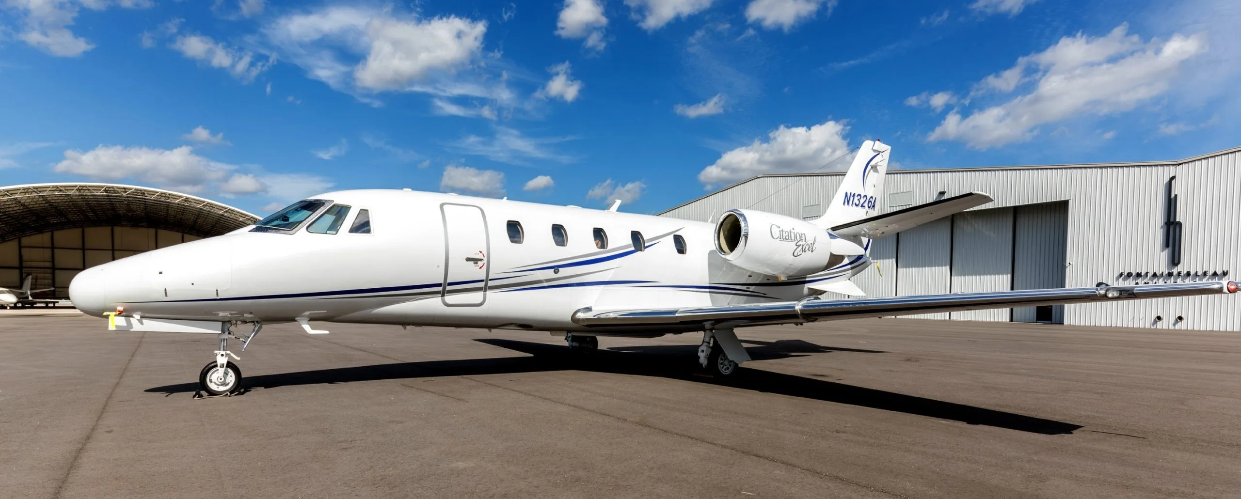 A white Citation Excel aircraft with blue stripes parked on the tarmac.