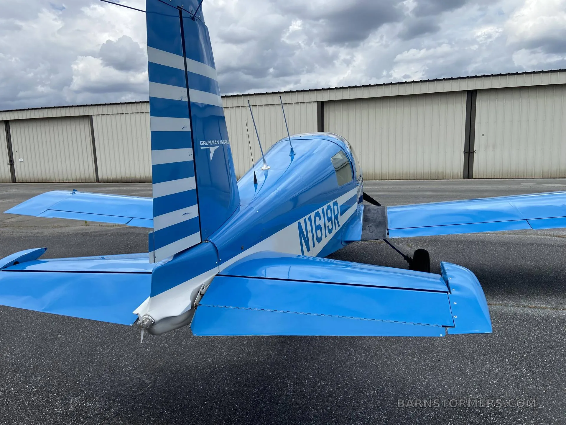 A rear view of a blue Grumman American aircraft (N1619R) with white stripes parked on the tarmac.