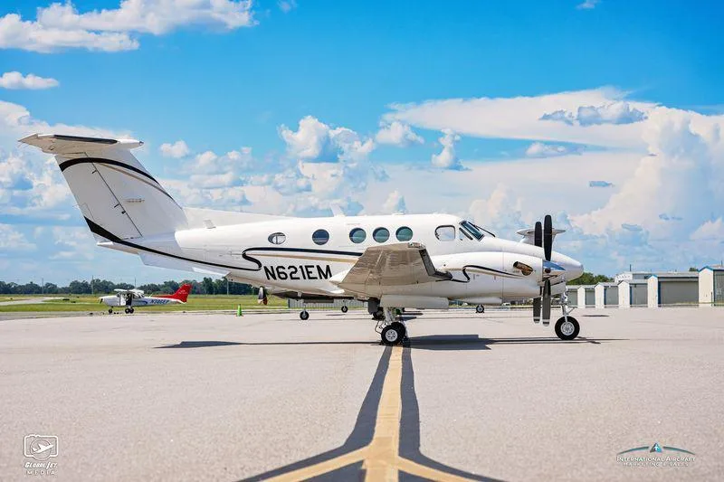 Side view of a white twin-engine turboprop aircraft, N621EM, with black and gold accents parked on a tarmac.
