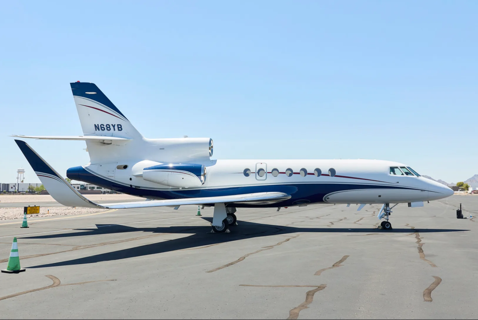 A white and blue business jet, N68YB, is parked on an airport tarmac under a clear sky.