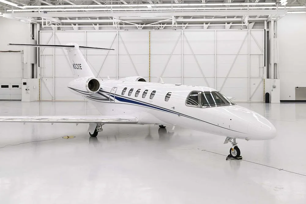 A front-right view of the white business jet N32GE with blue and grey stripes, parked in a hangar.