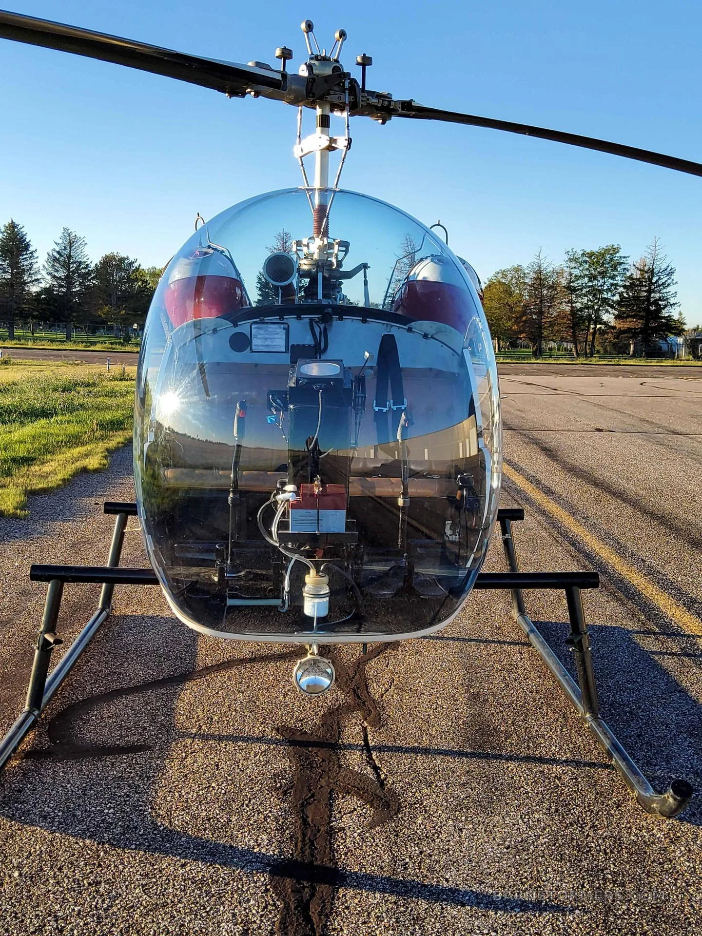 A view from the cockpit of a helicopter, showing the instrument panel and a runway stretching into the distance.