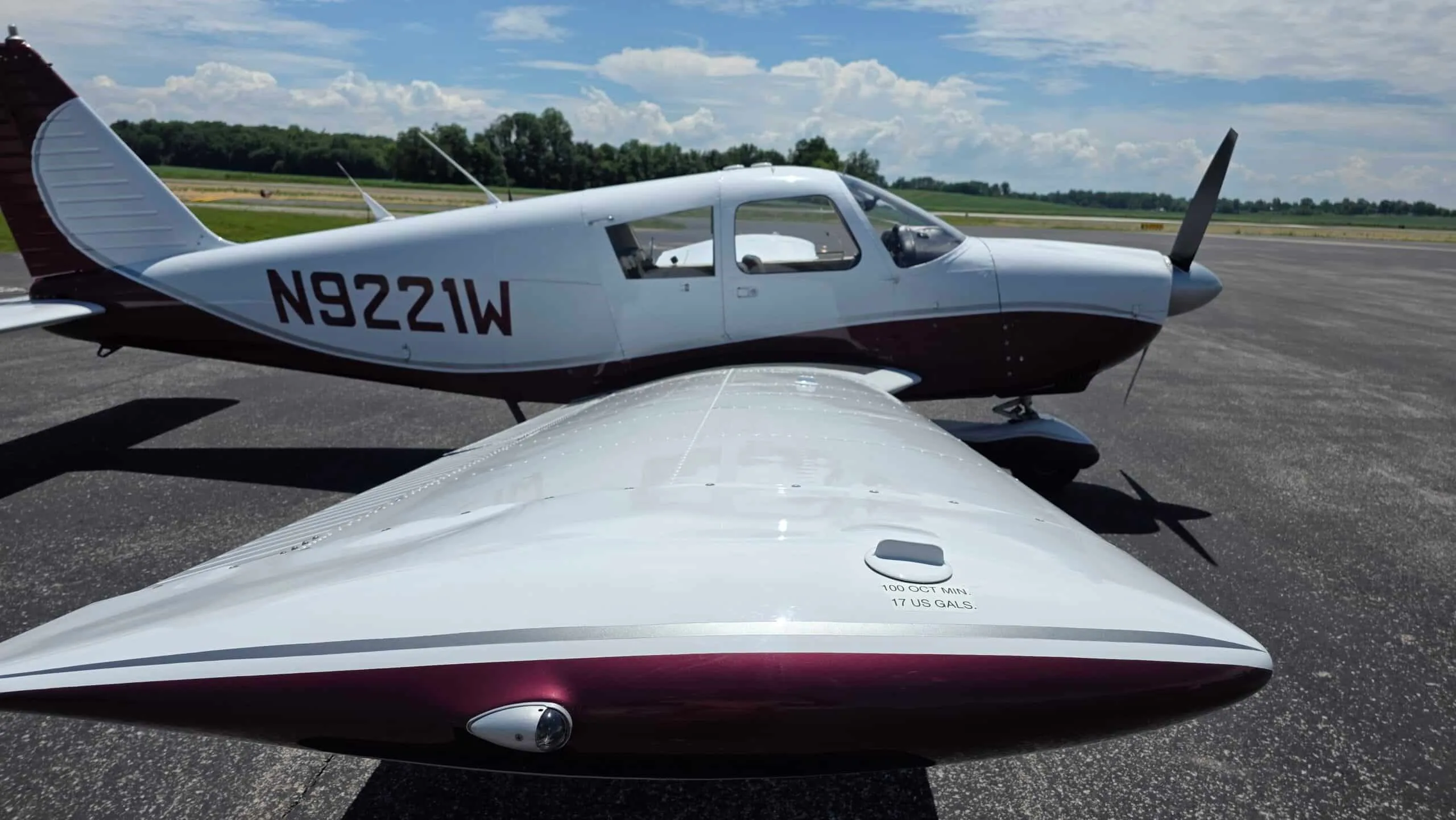 A view over the right wing of a white and maroon Piper Cherokee (N9221W) showing fuel tank markings.