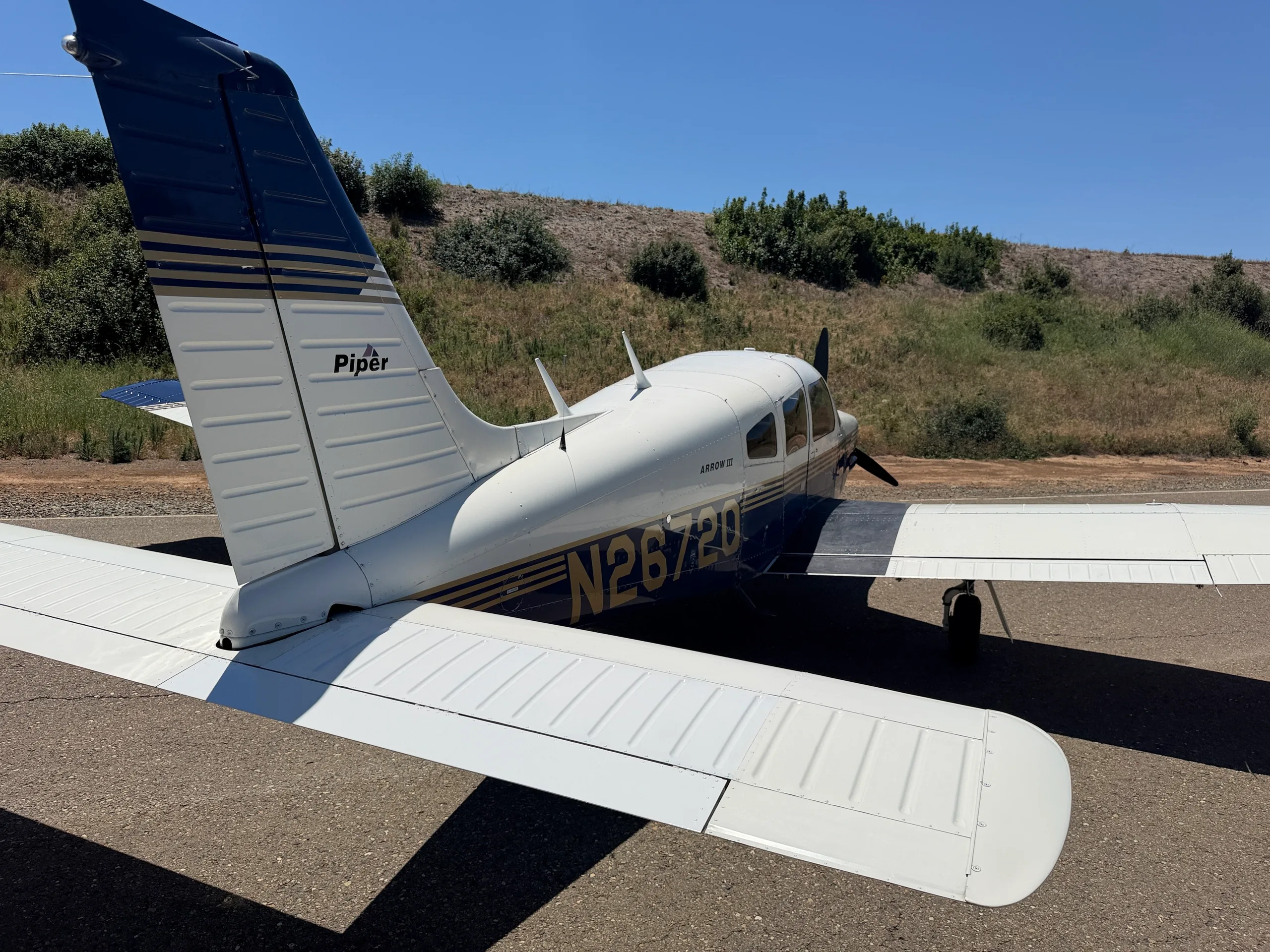 A rear-quarter view of the white and blue Piper Arrow III aircraft, tail number N2672Q, showing the tail and right wing.